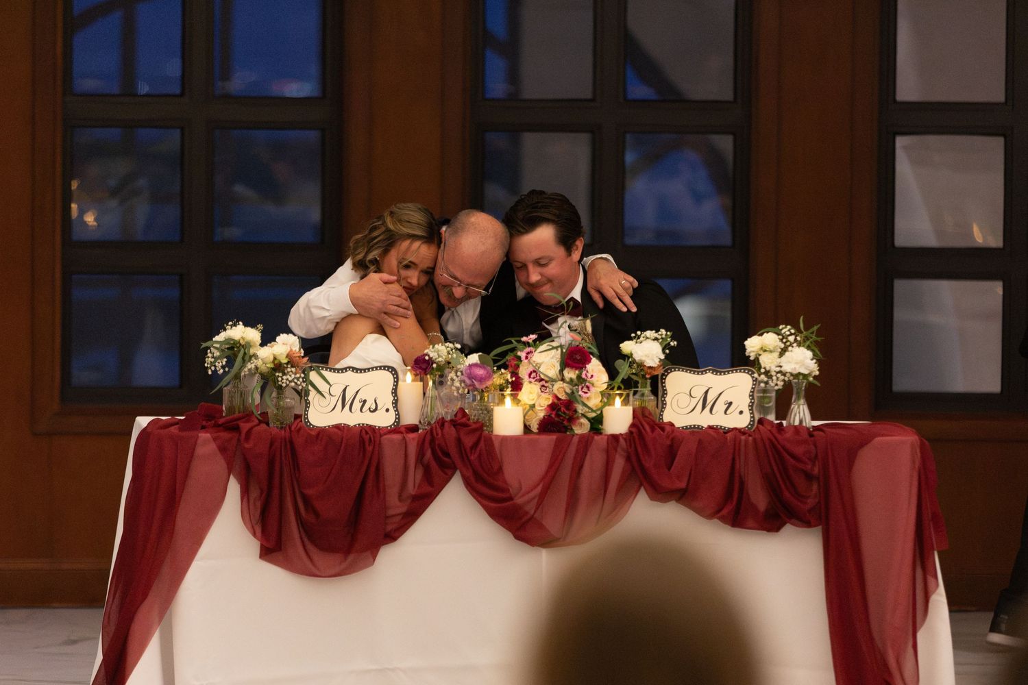 Bride and groom sharing an intimate moment at sweetheart table decorated with burgundy linens and floral arrangements.