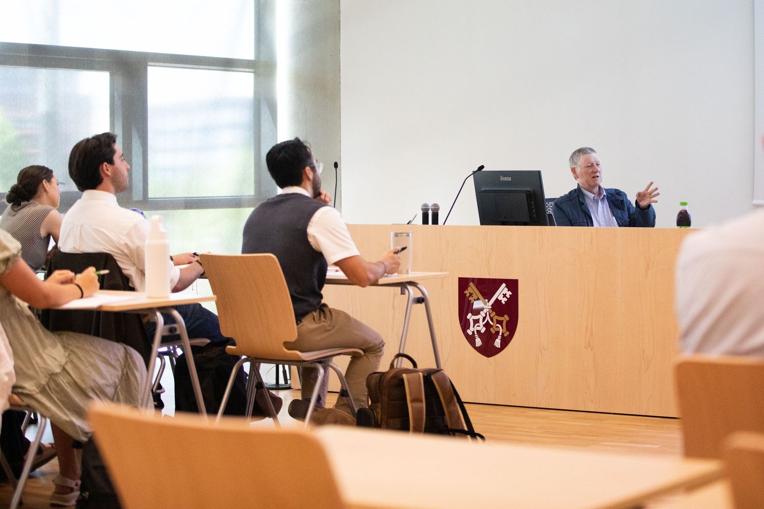 Professor lecturing at a wooden podium to attentive students in a modern university lecture hall.