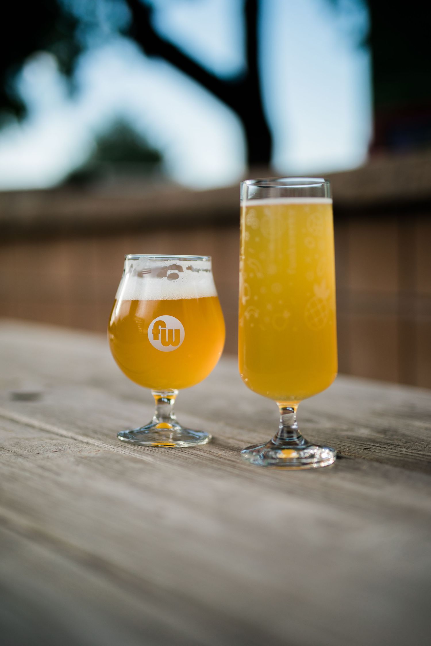 Two glasses of hazy craft beer sitting on a wooden surface with soft focus background.