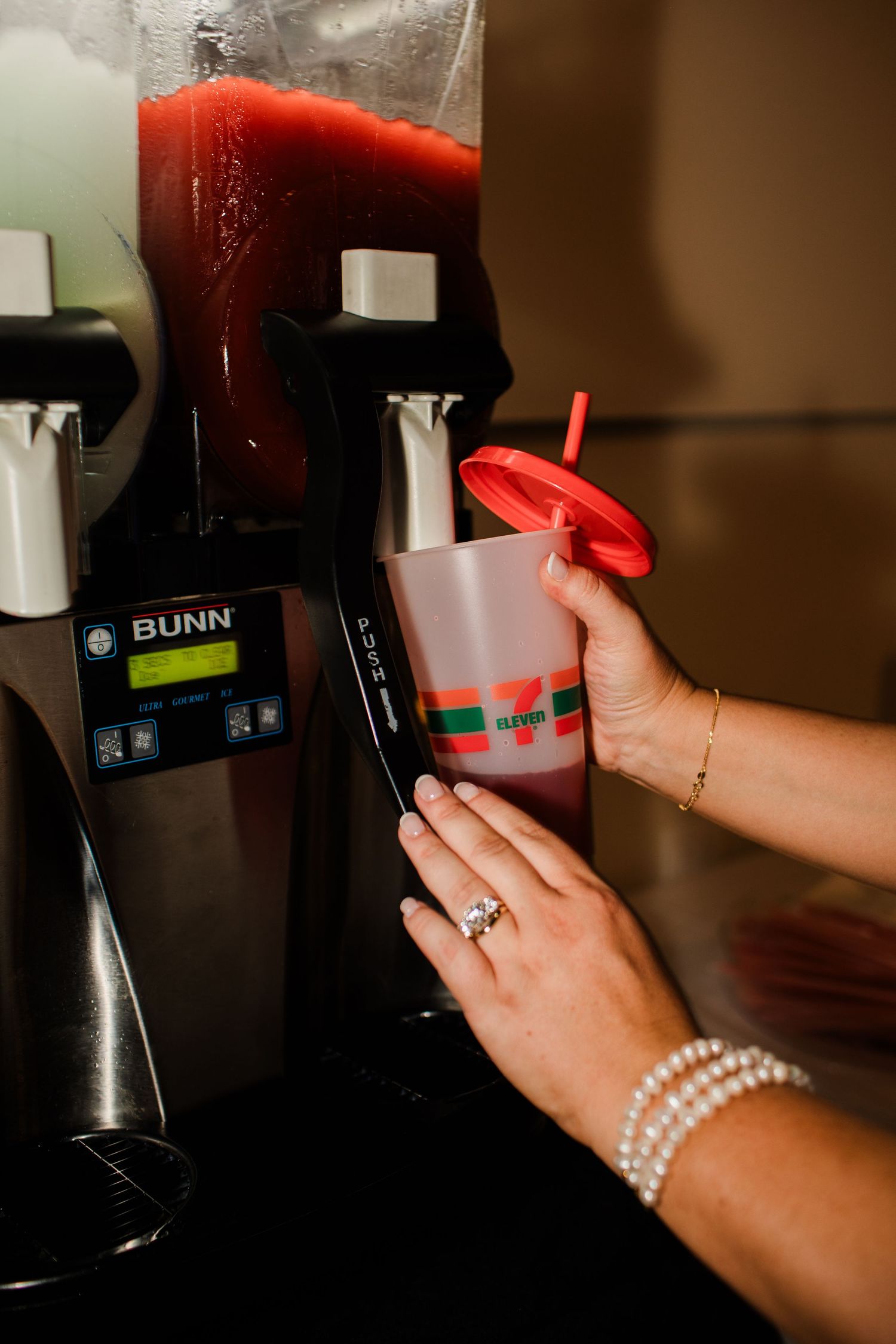 Bride fills 7-Eleven Slurpee cup at BUNN machine, wearing pearl bracelet and engagement ring.