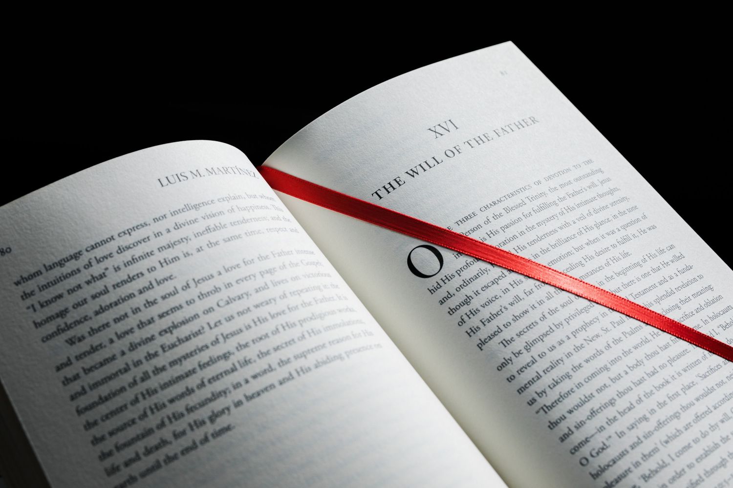 Open book with red ribbon bookmark on dark background, showing chapter XVI titled The Will of the Father.