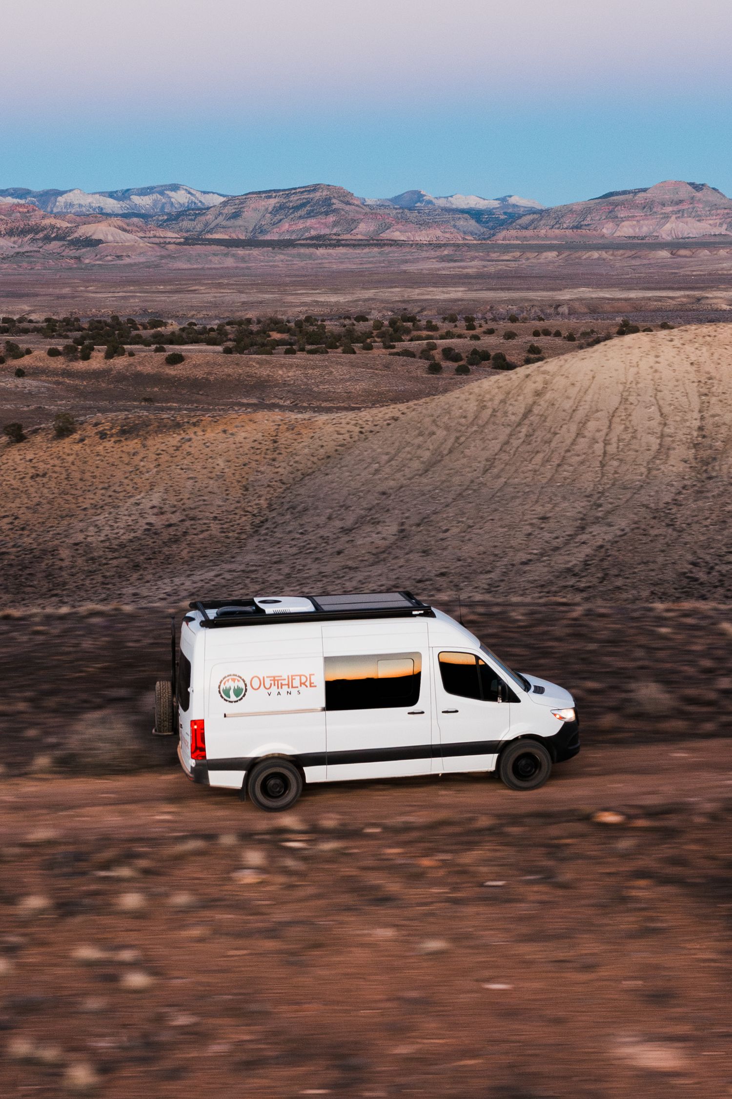 White commercial vans driving through a desert landscape with mountains in the background.