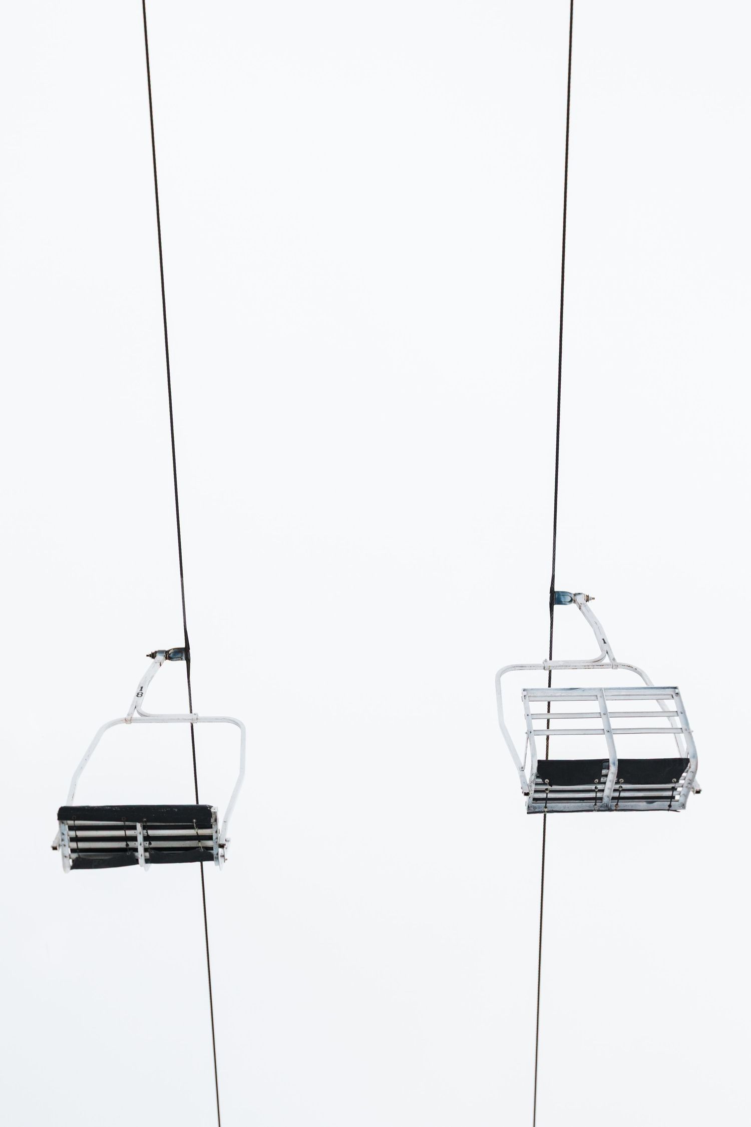 Empty ski lift chairs hang suspended against a white misty background creating a minimalist winter scene composition.