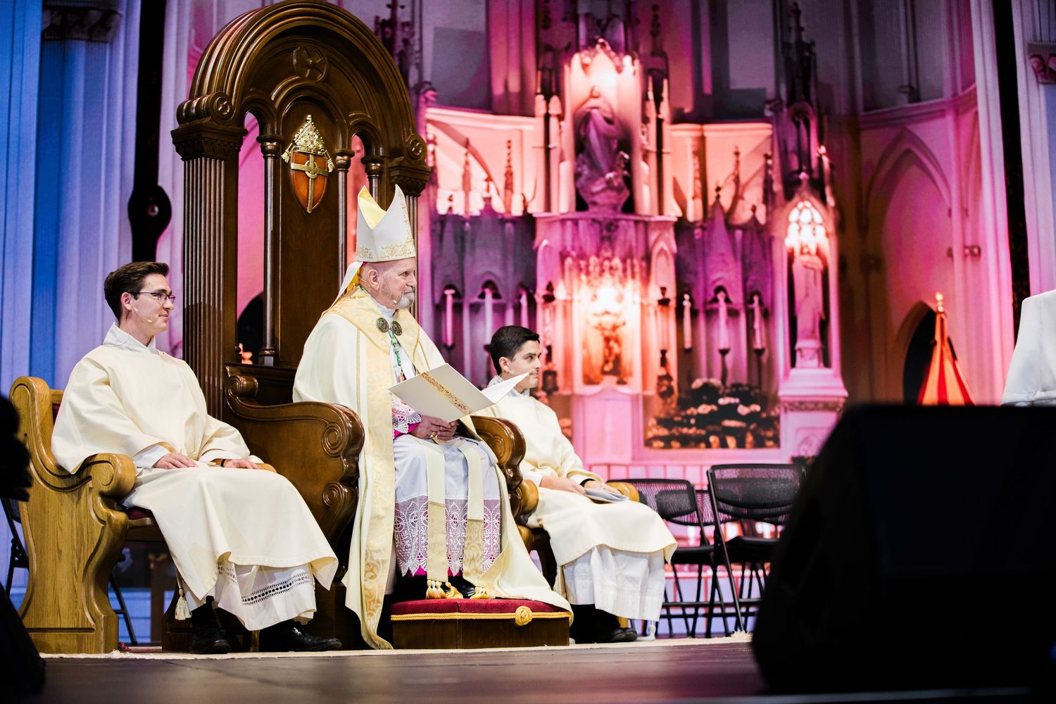 Cathedral interior illuminated with pink and blue lighting during a religious service.