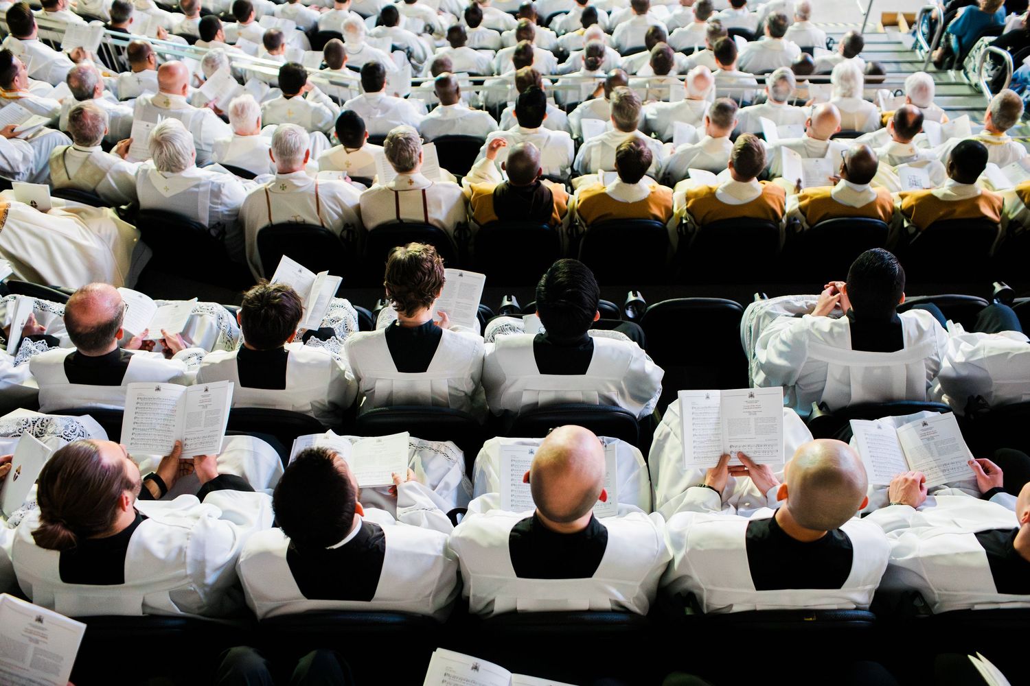 Medical students wearing white coats sit in tiered rows during a lecture in an academic auditorium.
