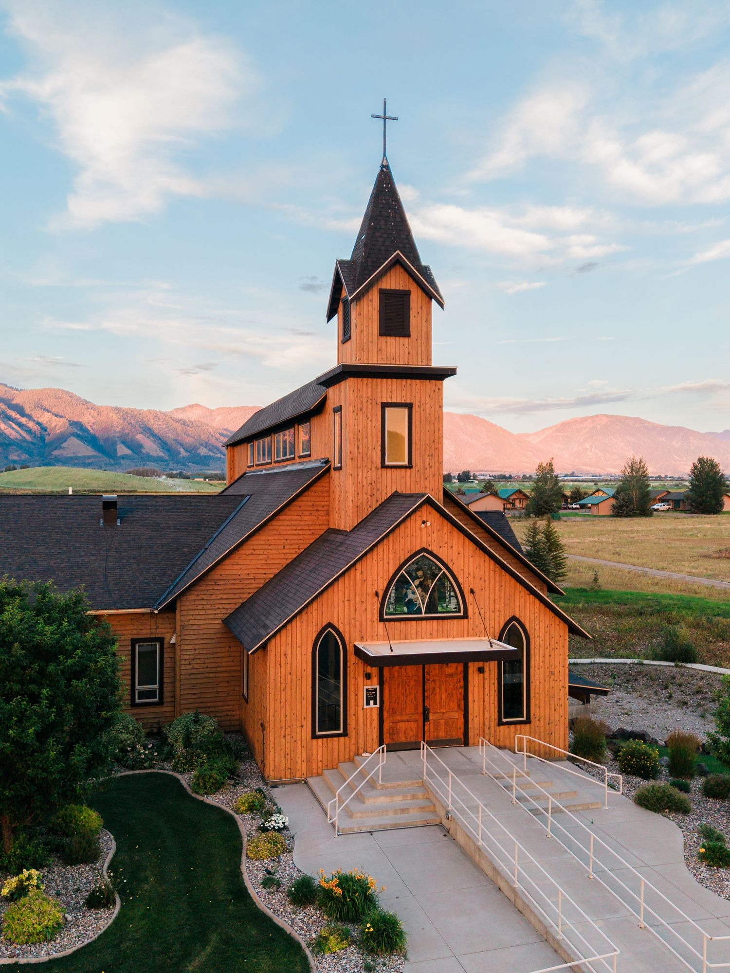 Wooden church with steeple and cross set against Montana mountains at sunset golden hour.
