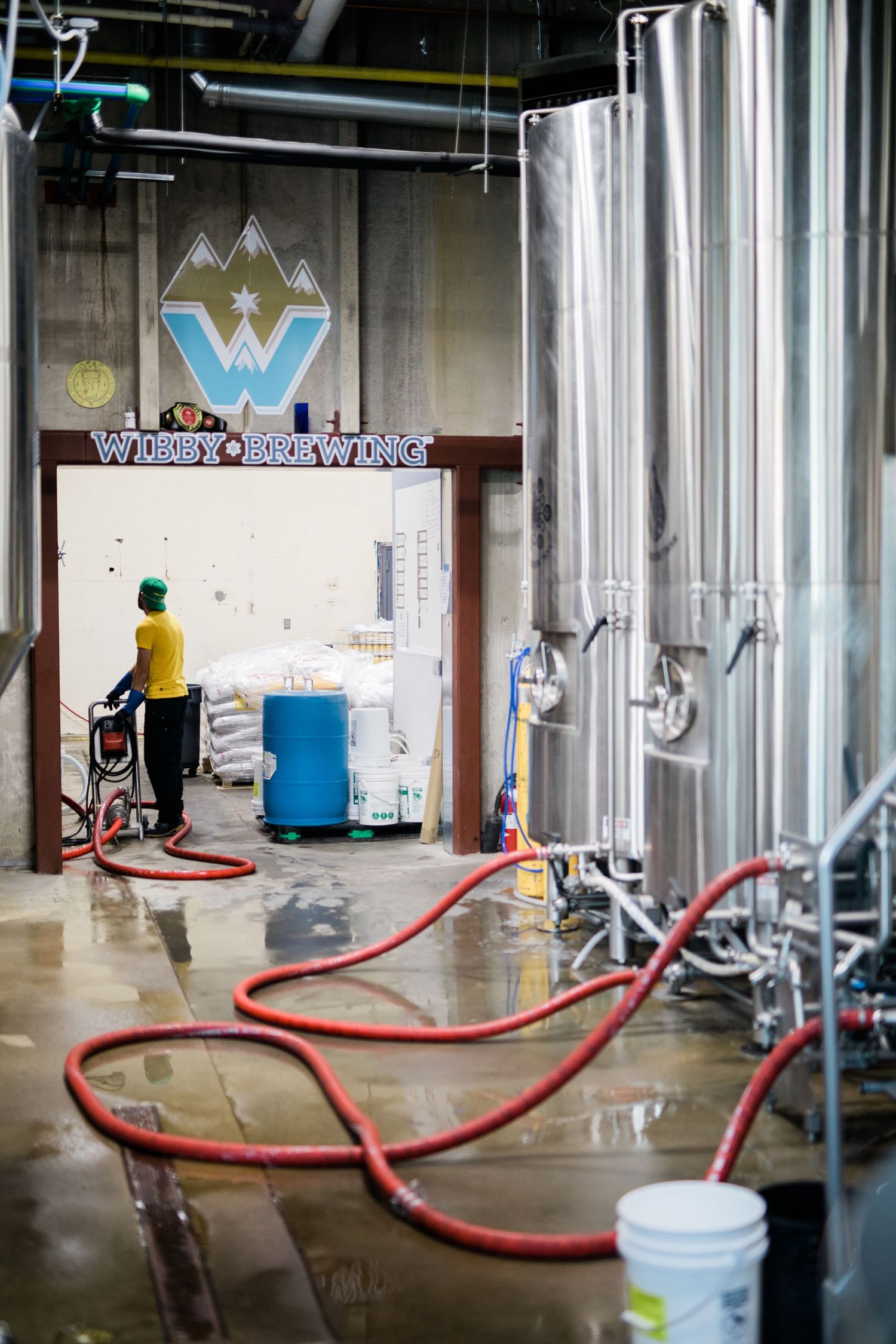 Industrial brewing equipment with red hoses and stainless steel tanks in a modern brewery.