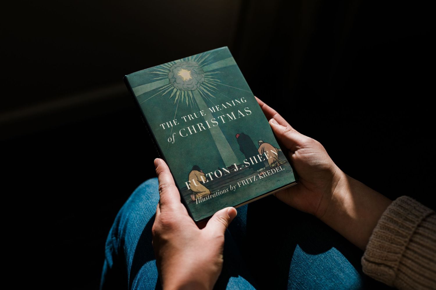 Hands holding a teal-colored hardcover book against a dark background.