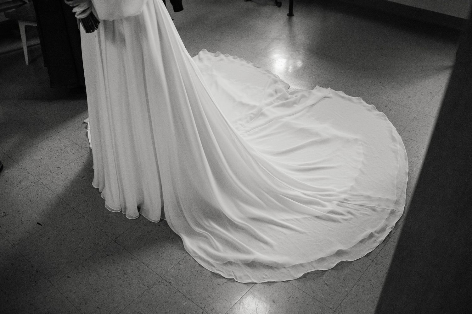 Black and white photos showing the flowing train of a wedding dress against dark flooring.