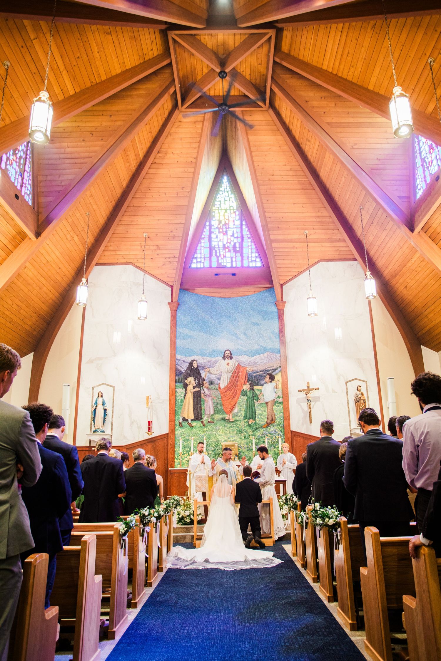 Wedding ceremony taking place in a beautiful wooden church with vaulted ceilings and stained glass windows.