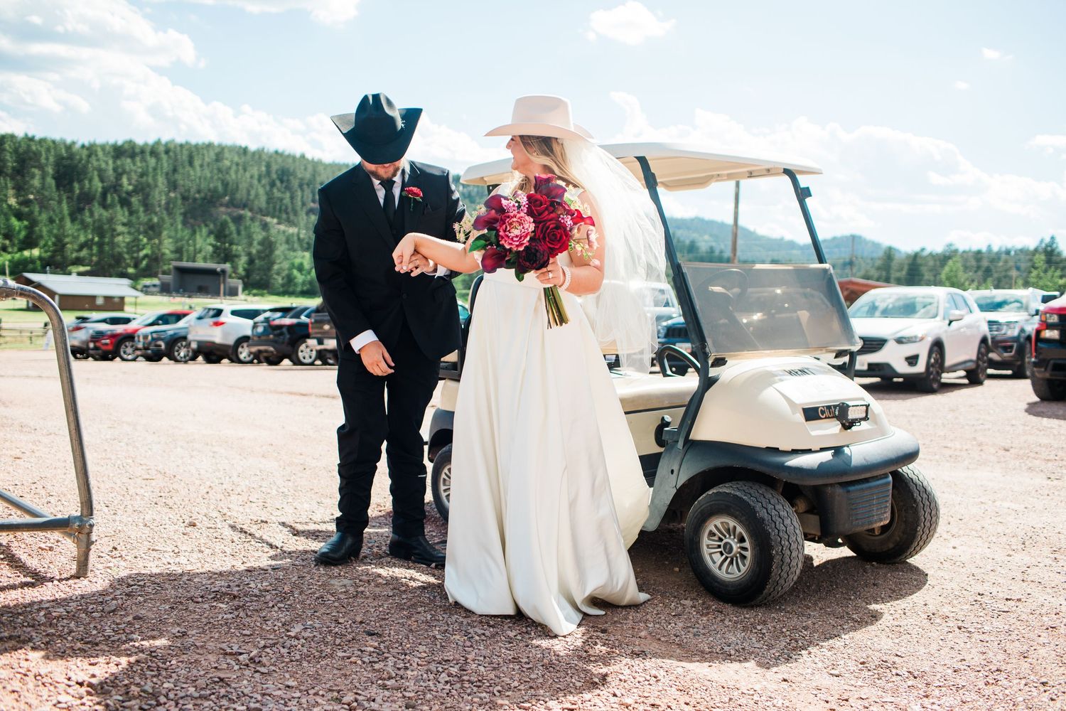 Bride and groom in cowboy hats share a moment beside a golf cart at outdoor wedding venue.