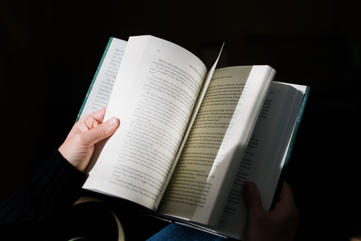 Hands holding open a book with pages illuminated against a dark background.