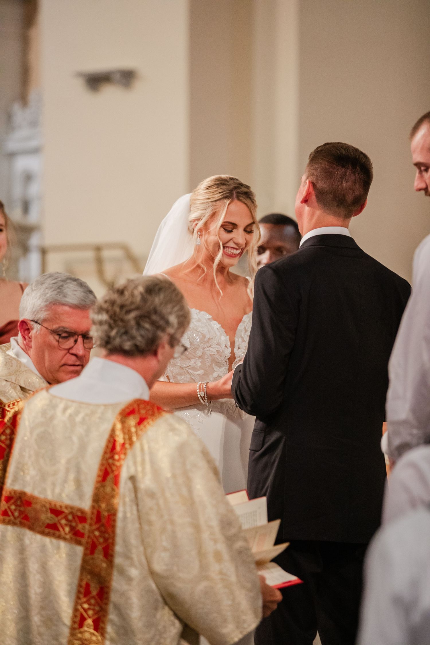 Smiling bride in lace gown exchanges vows with groom at elegant church altar during wedding ceremony.