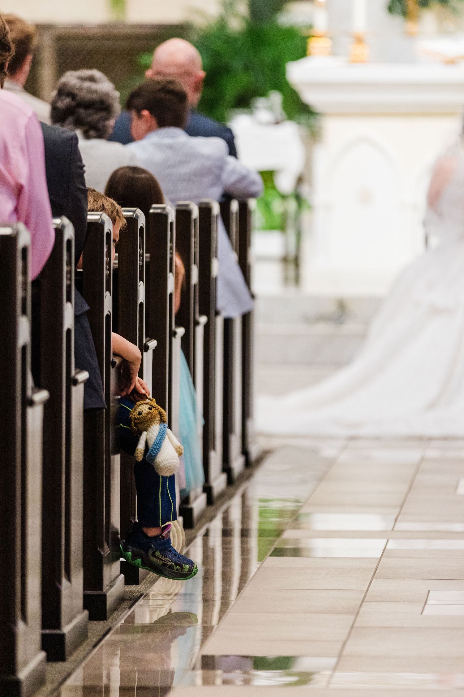 Child holding a toy stands by church pews during a wedding ceremony with a bride visible in the aisle.