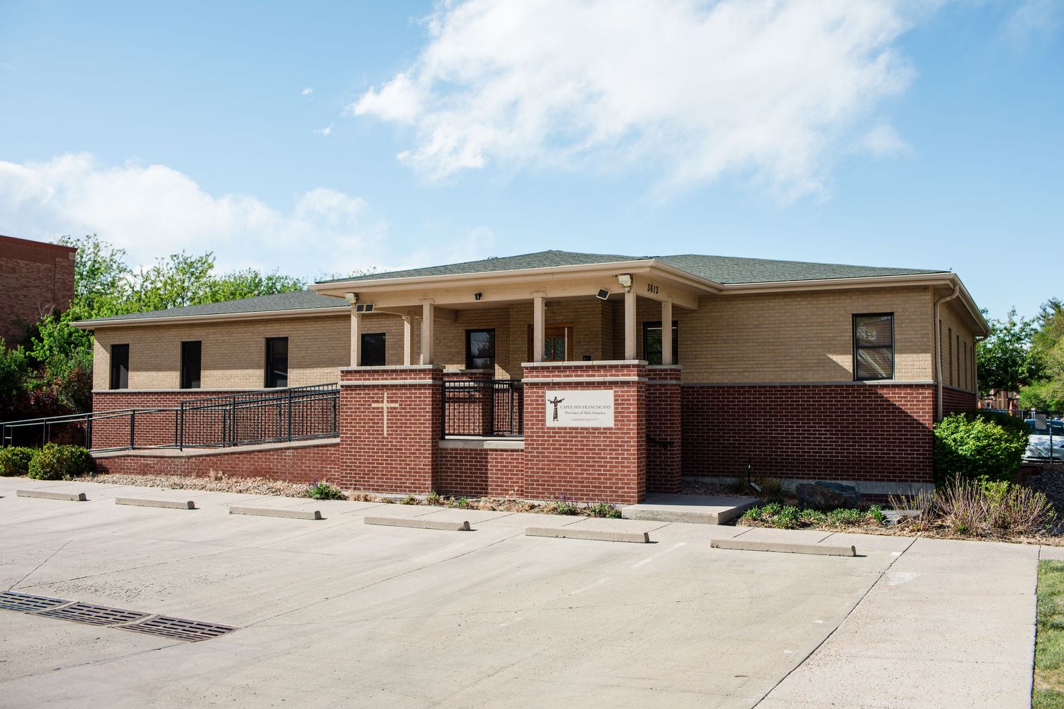 Brick church building with cross symbols, covered porch entrance, and parking lot on a sunny day.