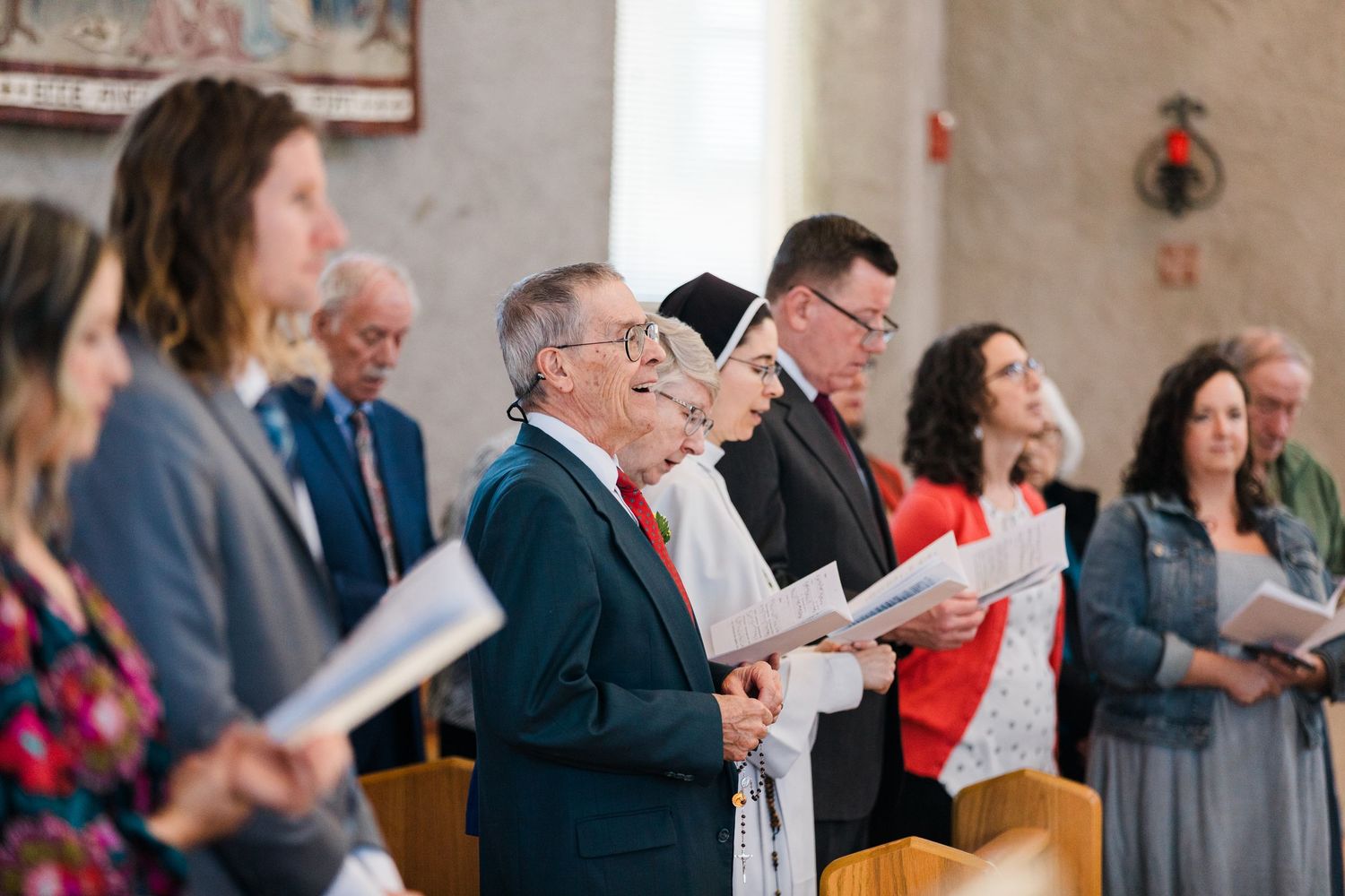 Congregation singing hymns from booklets during a church service inside a traditional chapel.