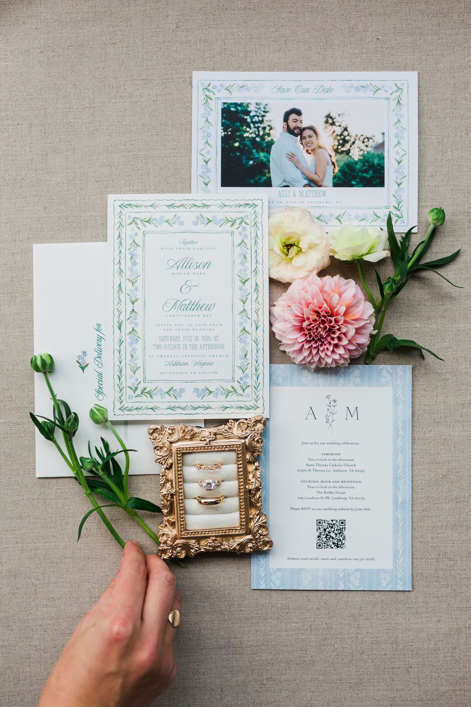 Elegant wedding invitation suite with floral decor, couple photo, rings in gold frame, and pink dahlia on linen background.