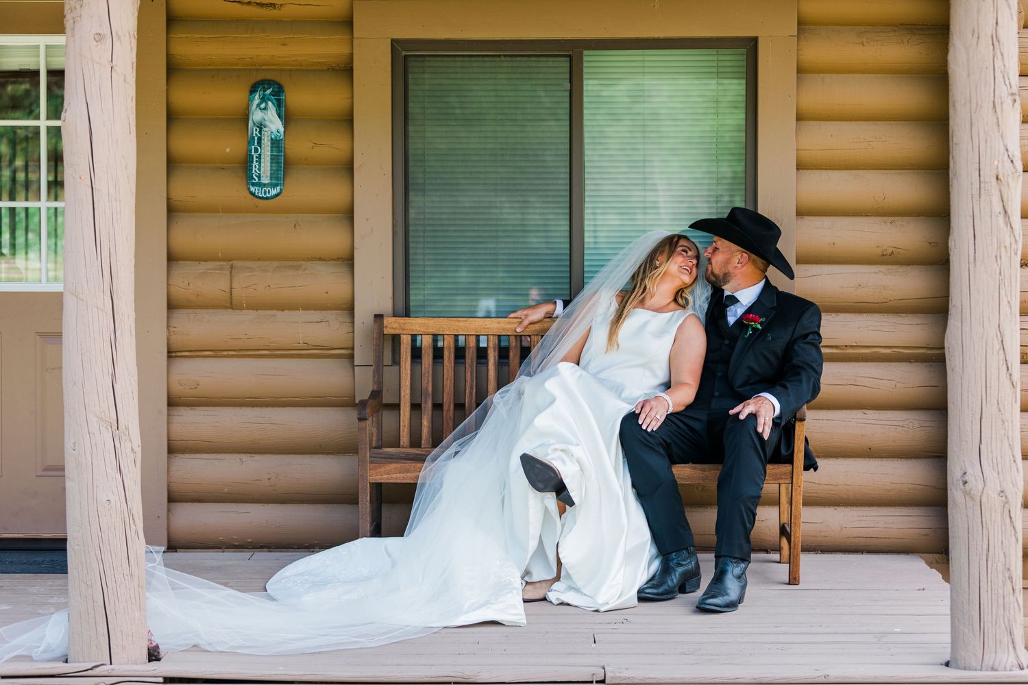 Bride and groom sharing a romantic moment on a wooden cabin porch, groom wearing a black cowboy hat.