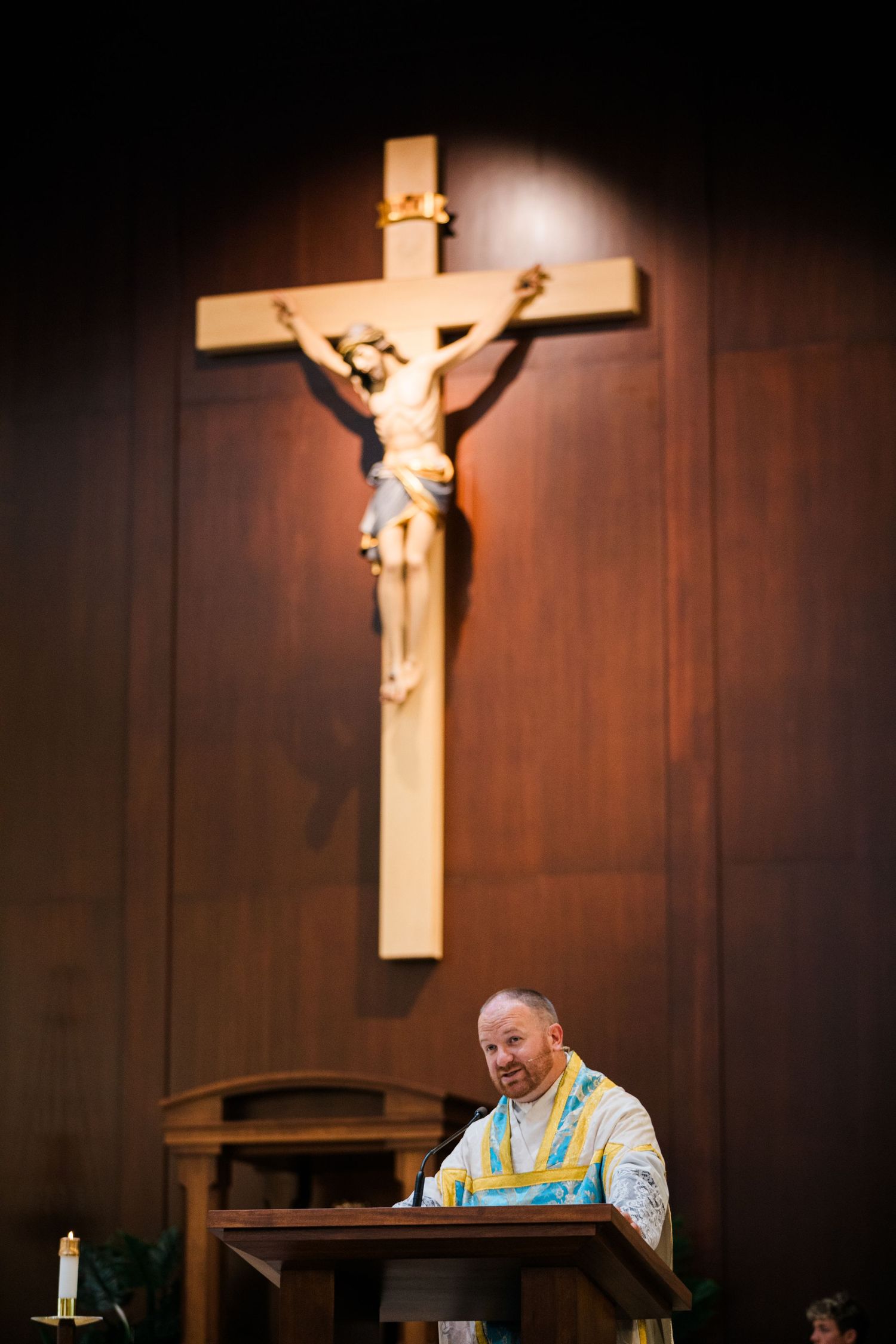 A wooden crucifix hangs on a dark paneled wall in a church setting.