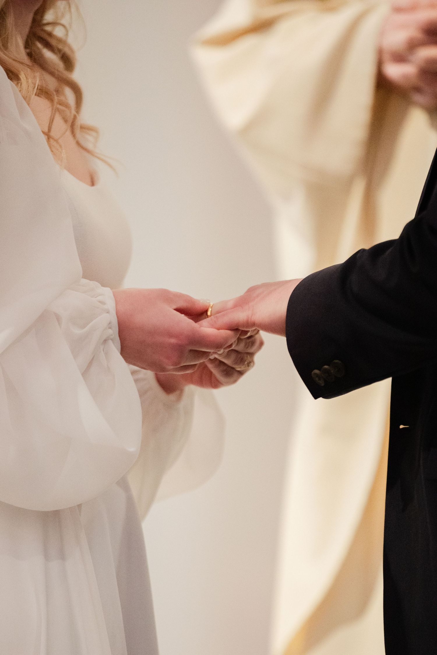 A close-up shot of hands exchanging rings during a wedding ceremony against a soft white background.