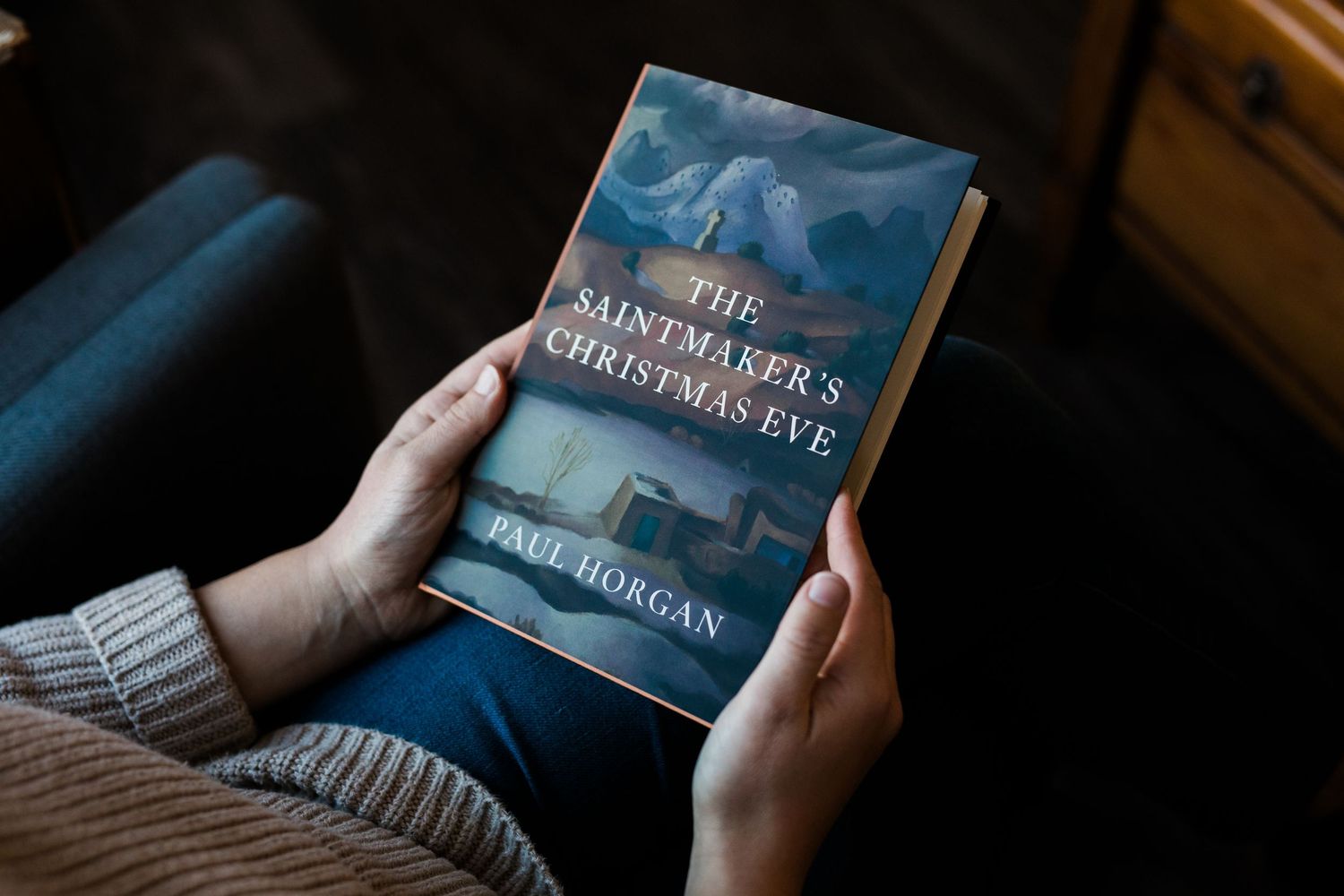 A person's hands hold a dark hardcover book against a moody blue background in a series of similar shots.