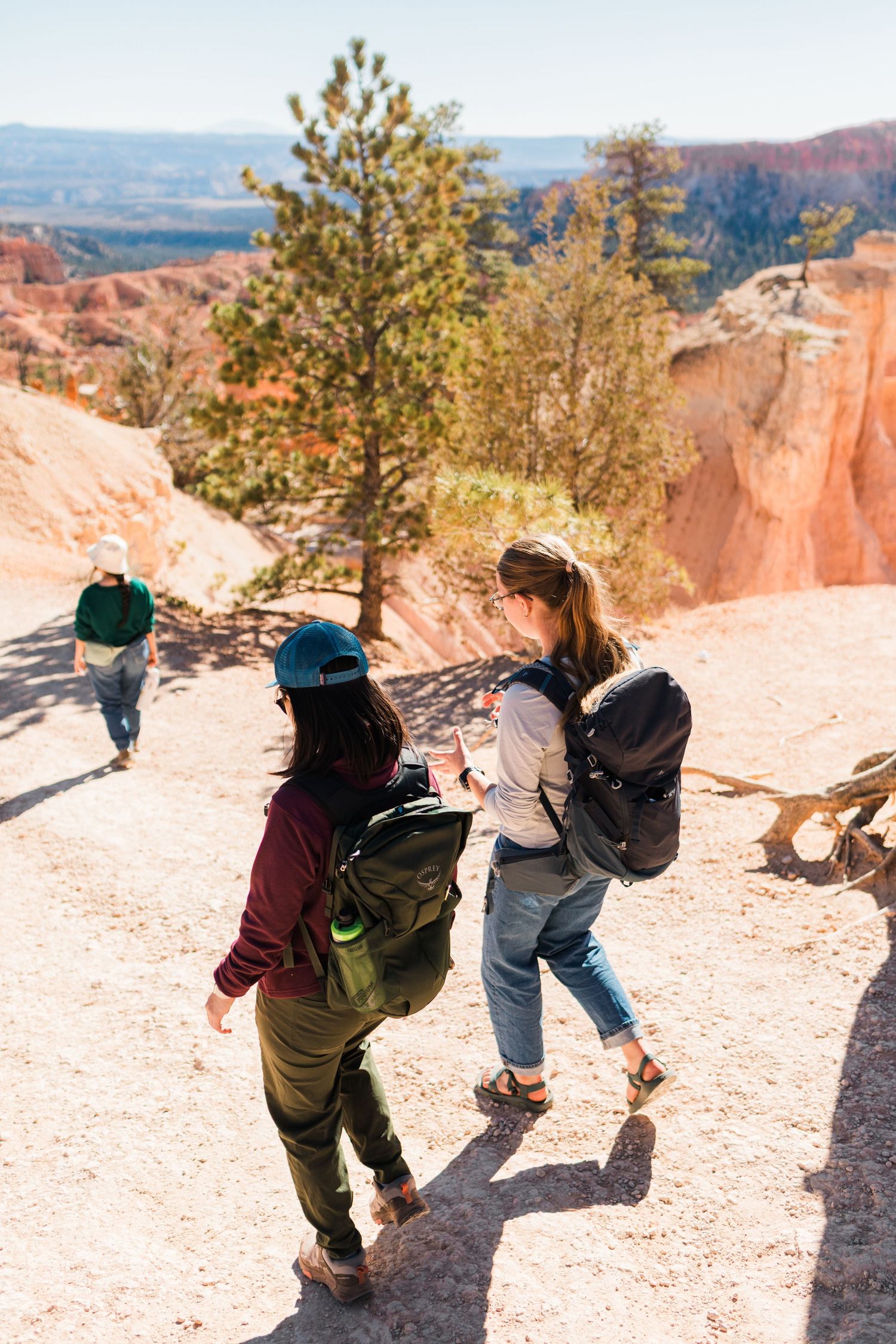 Three hikers lean over a scenic overlook at Bryce Canyon National Park with orange rock formations in the background.
