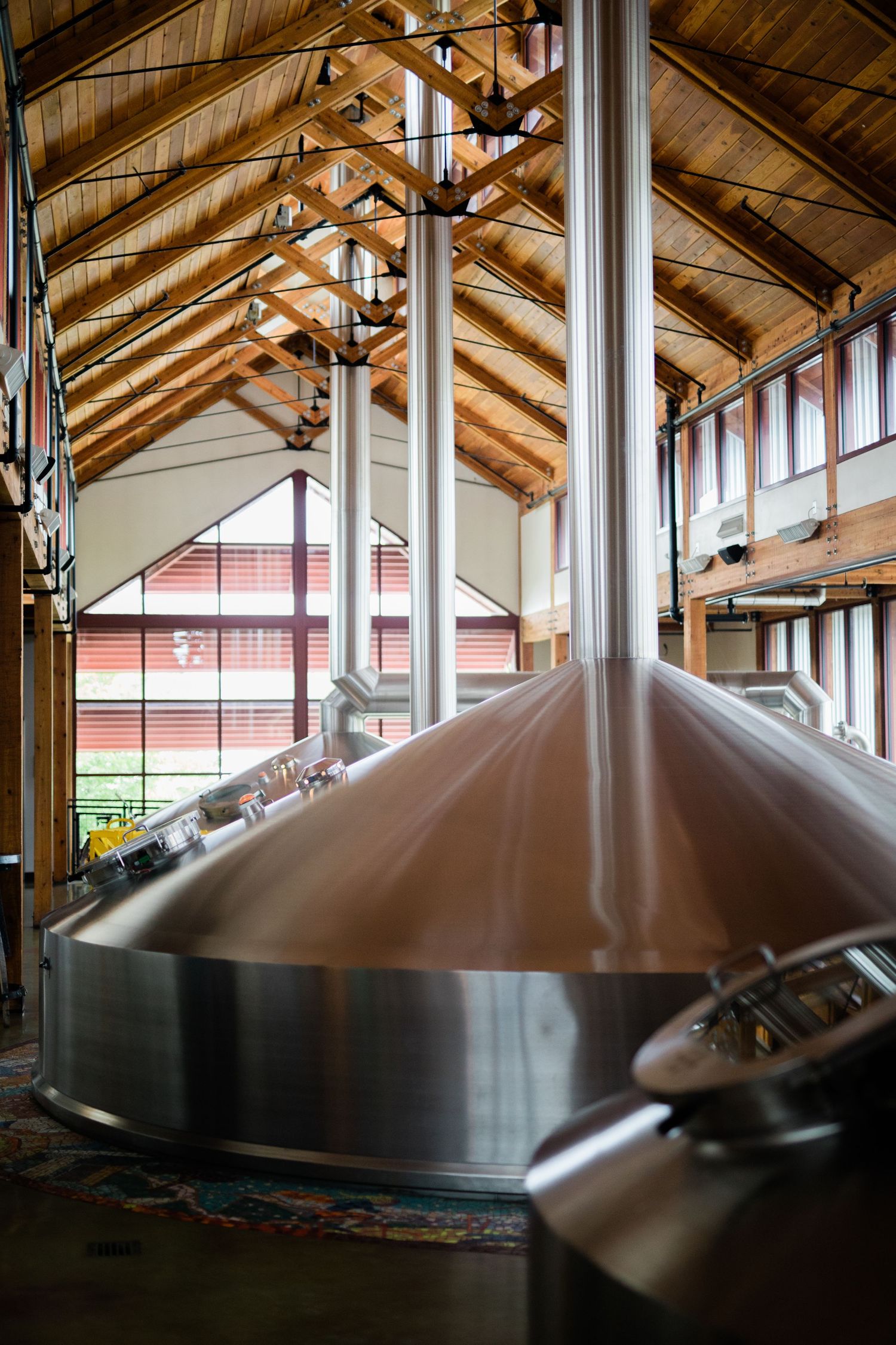 Large copper brewing kettles under wooden beams in a distillery production facility.