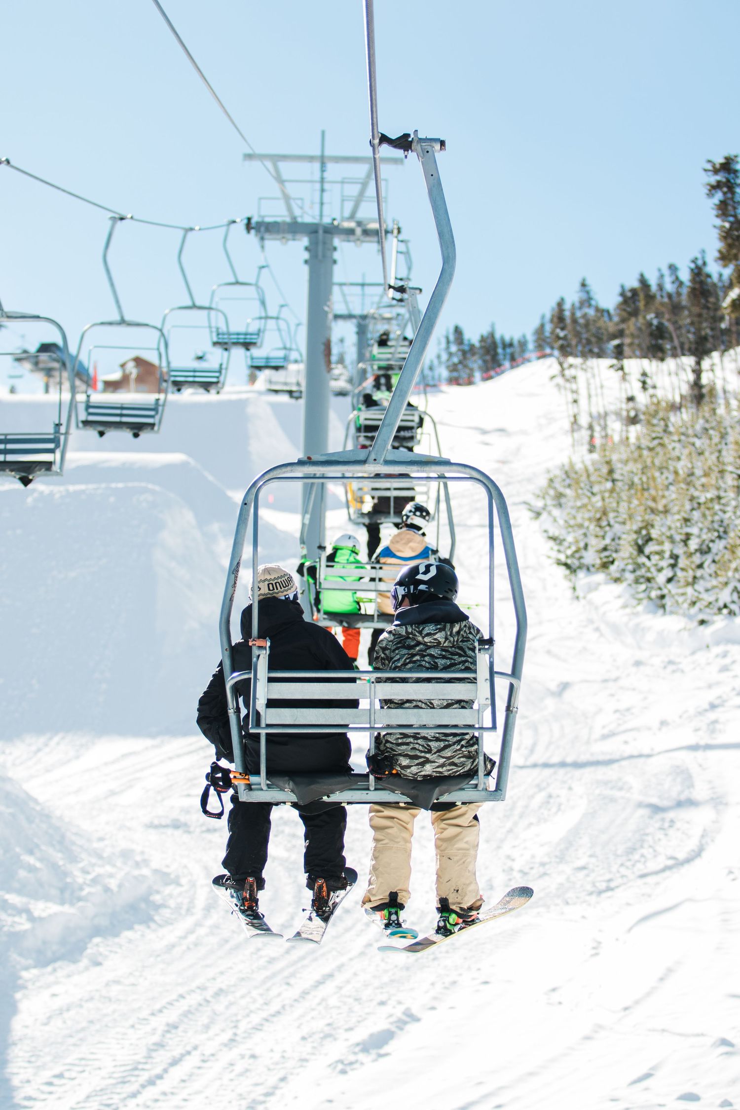 Skiers riding a chairlift at a snow-covered mountain resort on a sunny day.