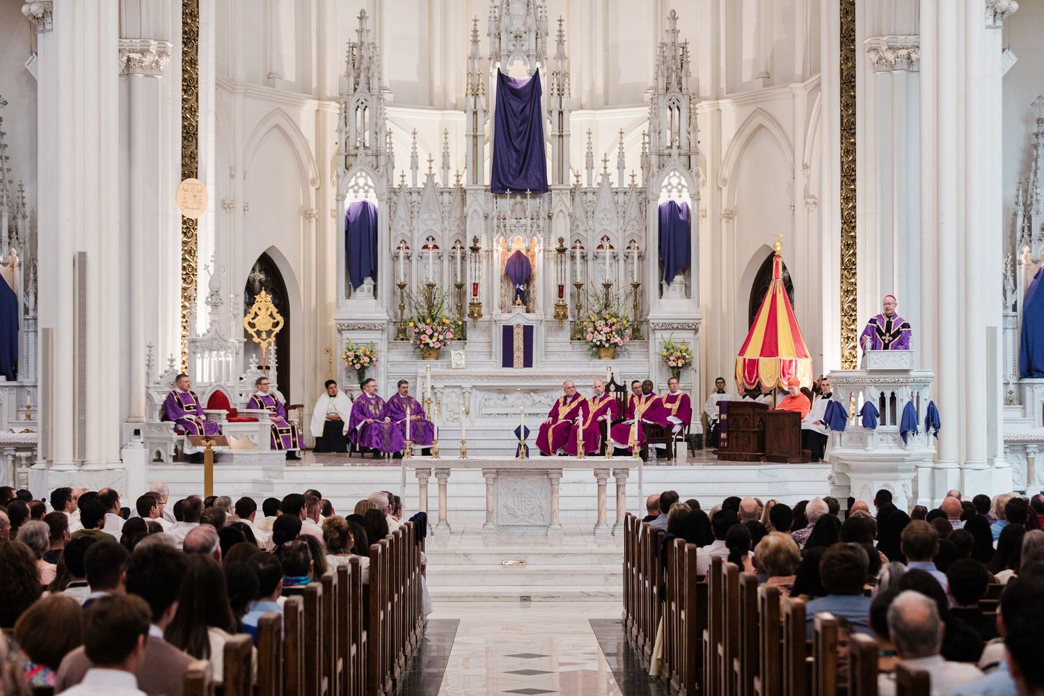 Wide view of a grand cathedral interior with ornate architecture and pews filled with attendees during a formal ceremony.