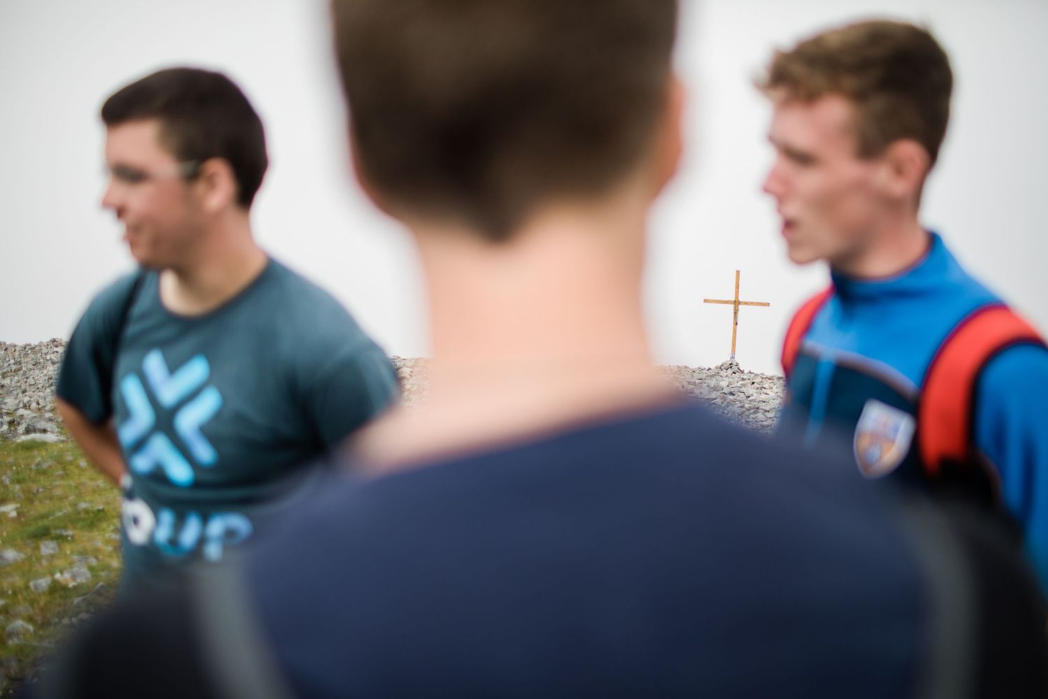 Two young men stand near a wooden cross on a rocky Irish mountaintop pilgrimage site.