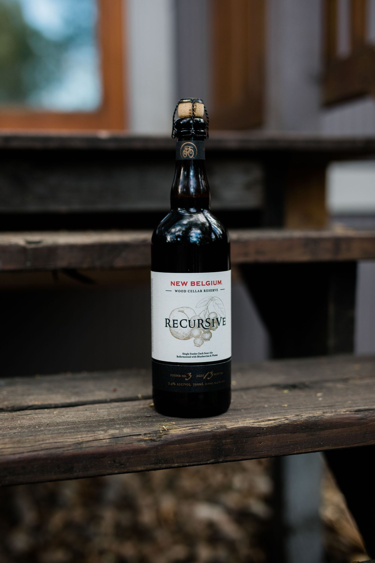 Artisanal beer bottles arranged on a rustic wooden shelf showing New Belgium and Recurso craft brewery labels.