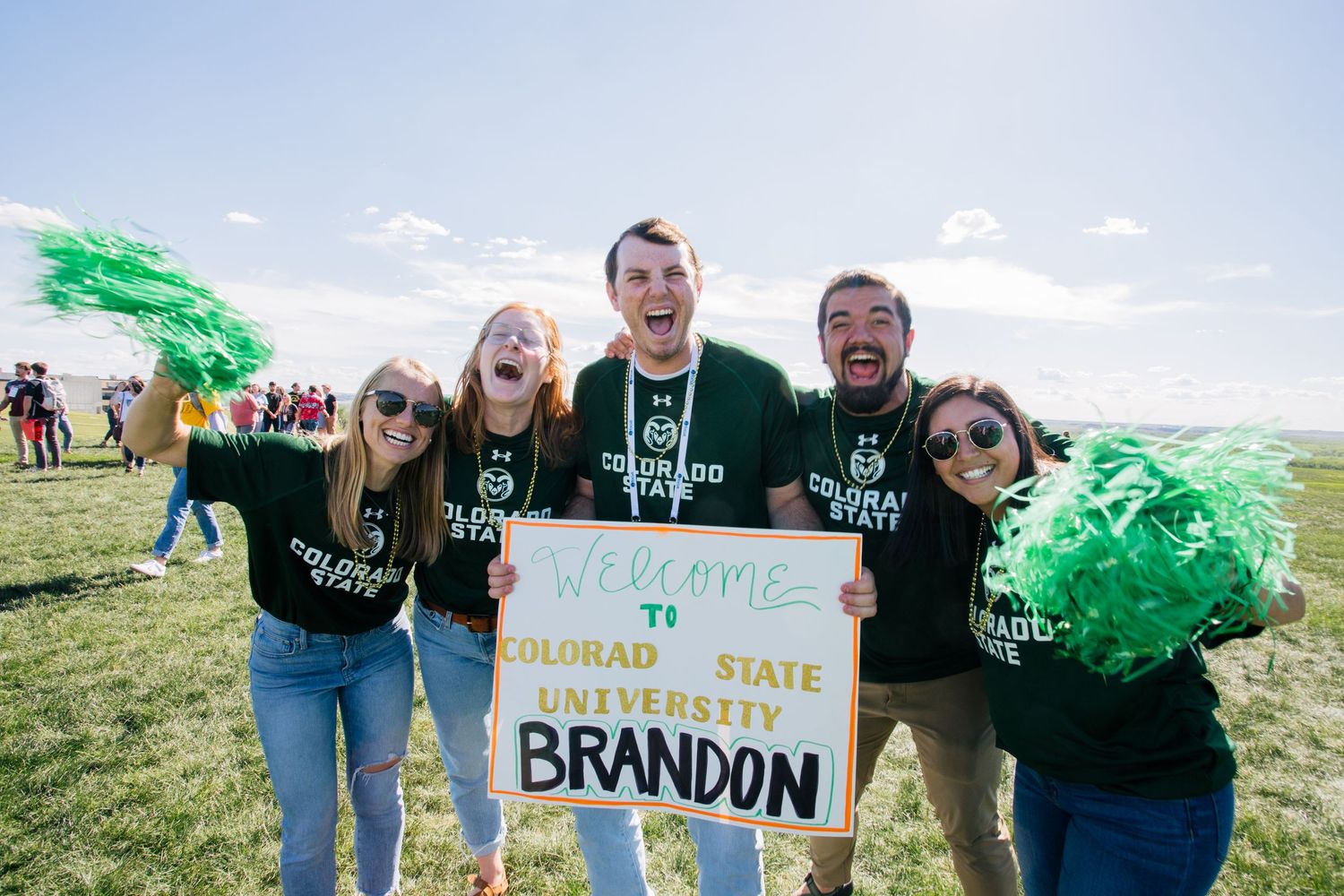 Group of students celebrating outdoors while holding colorful signs and banners at a university event.