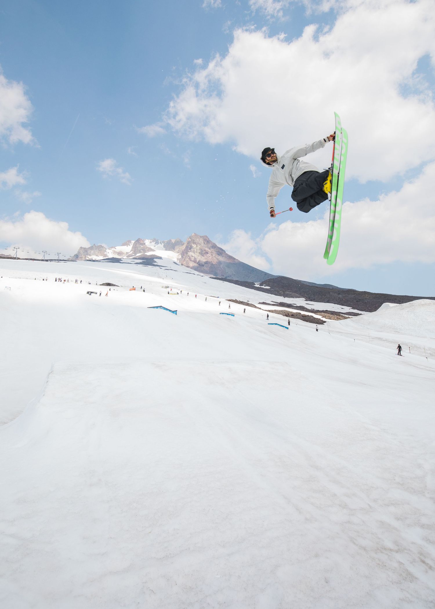 Freestyle skier performing aerial tricks and rotations in a terrain park with mountain peaks visible.