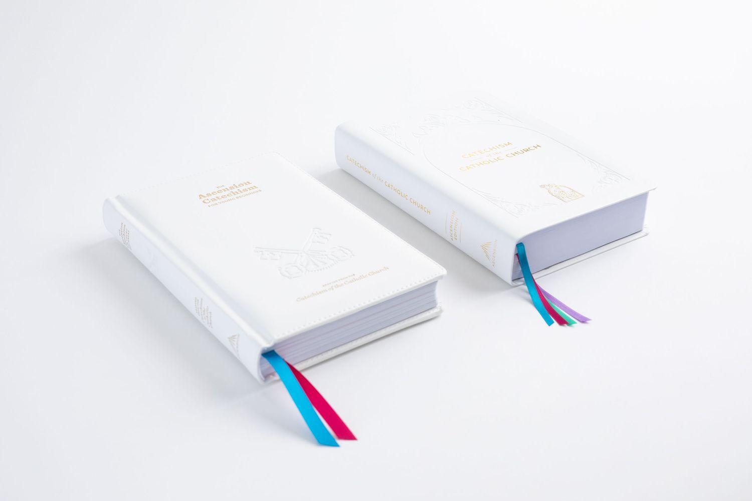 Two white hardcover books with colorful ribbon bookmarks on a white surface.
