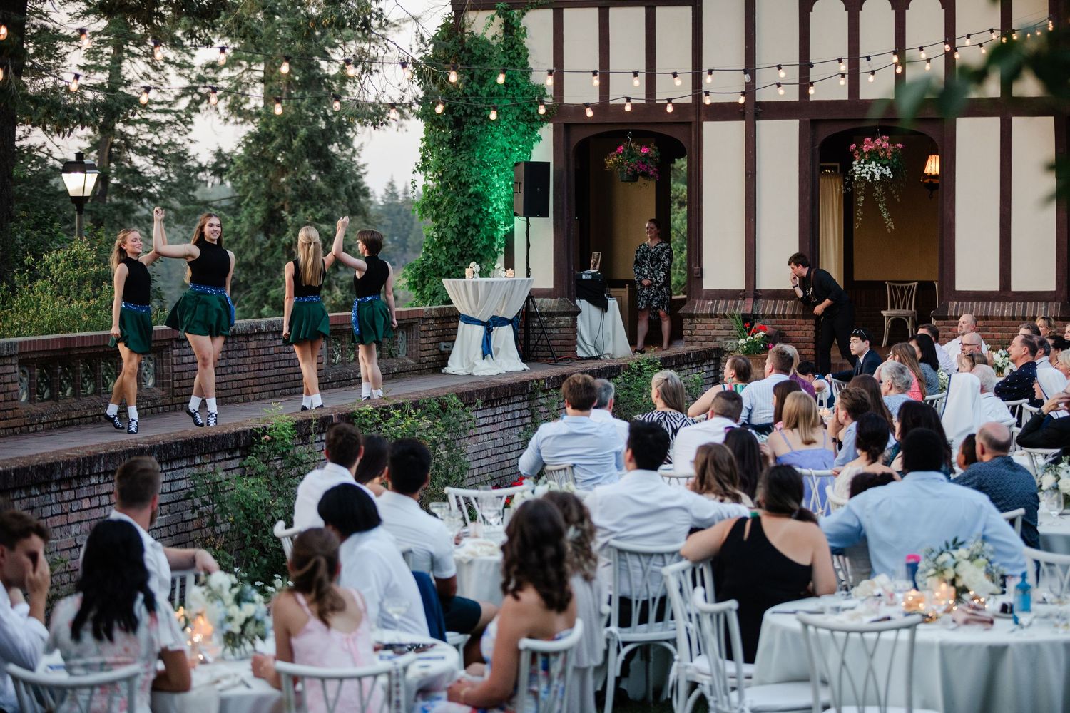 Irish dancers perform in green costumes for seated wedding guests at an elegant outdoor evening reception.