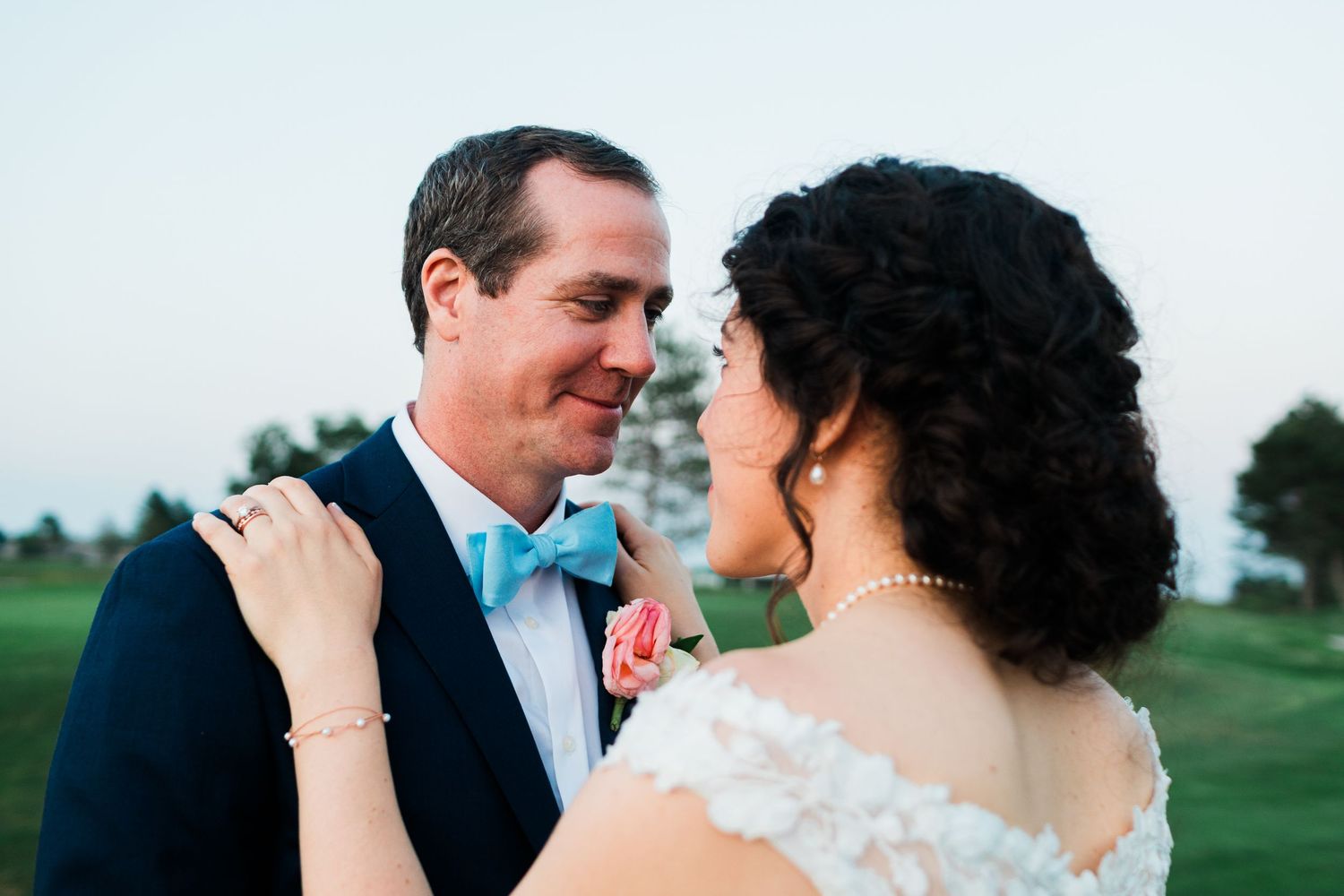 A bride and groom share a romantic moment outdoors, with the groom in a navy suit and blue bow tie.