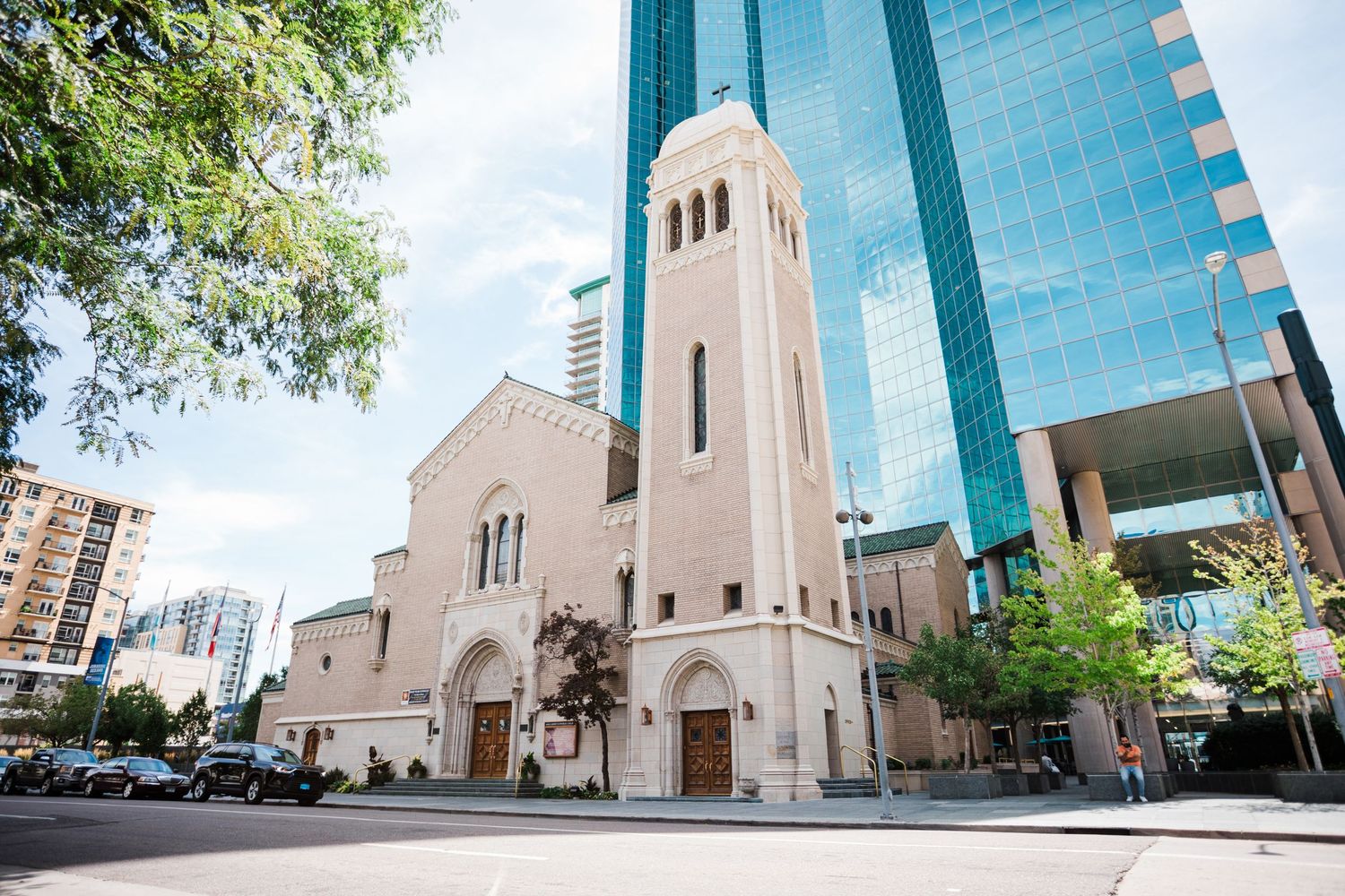 A large church building with a tall bell tower stands in front of modern high-rise buildings in an urban setting.