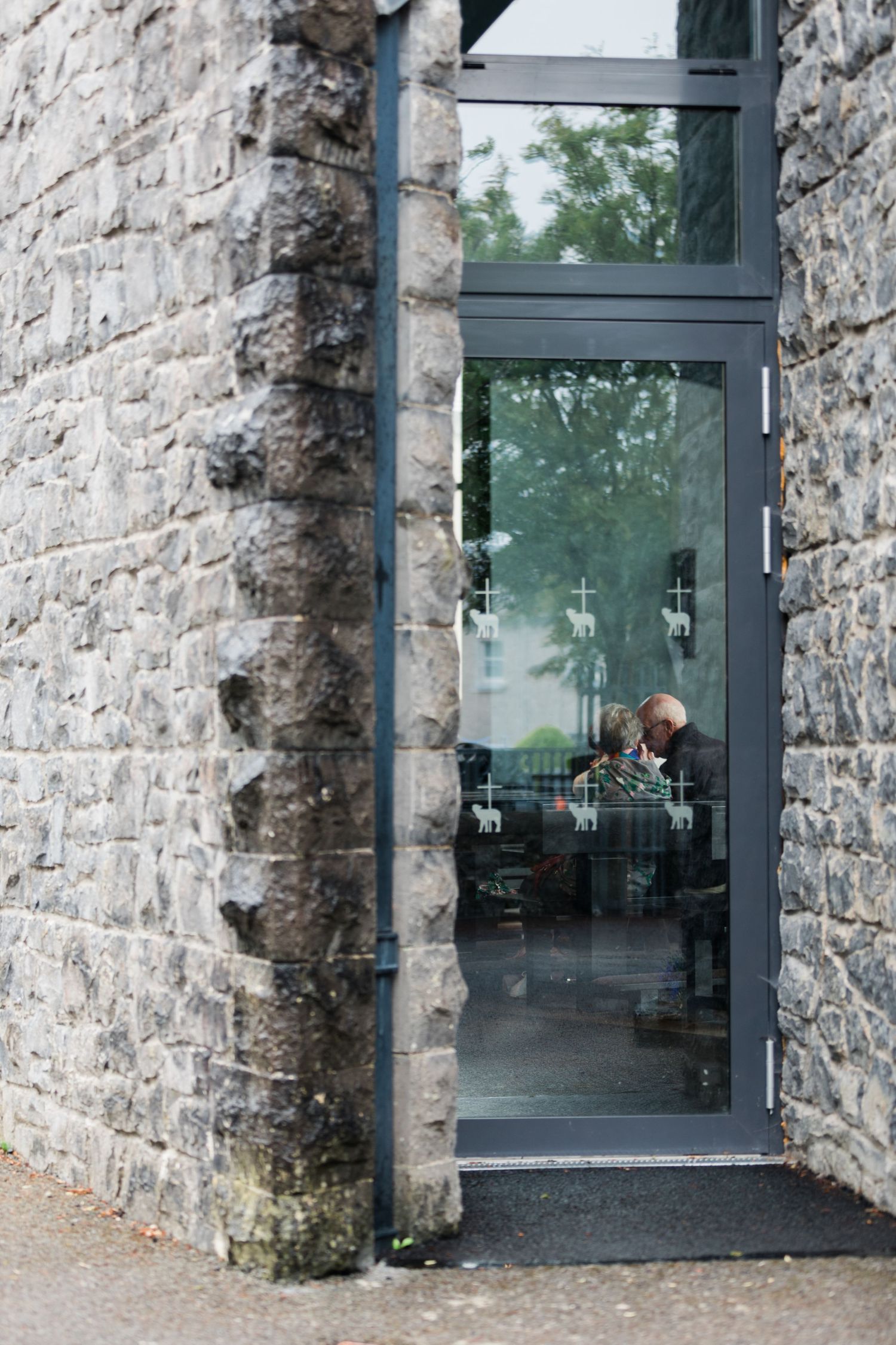 A man visible through a glass door set in a rustic stone wall building exterior.