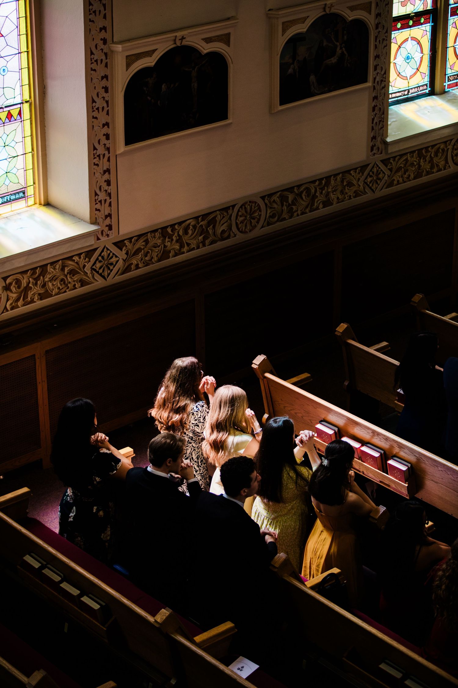 Aerial view of wedding guests seated in ornate church pews with colorful stained glass windows.
