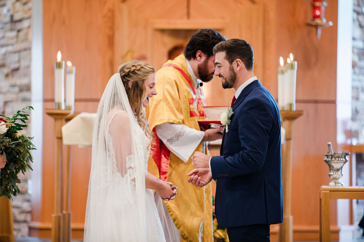 Bride and groom exchange rings during a traditional church wedding ceremony with an officiant in golden robes.