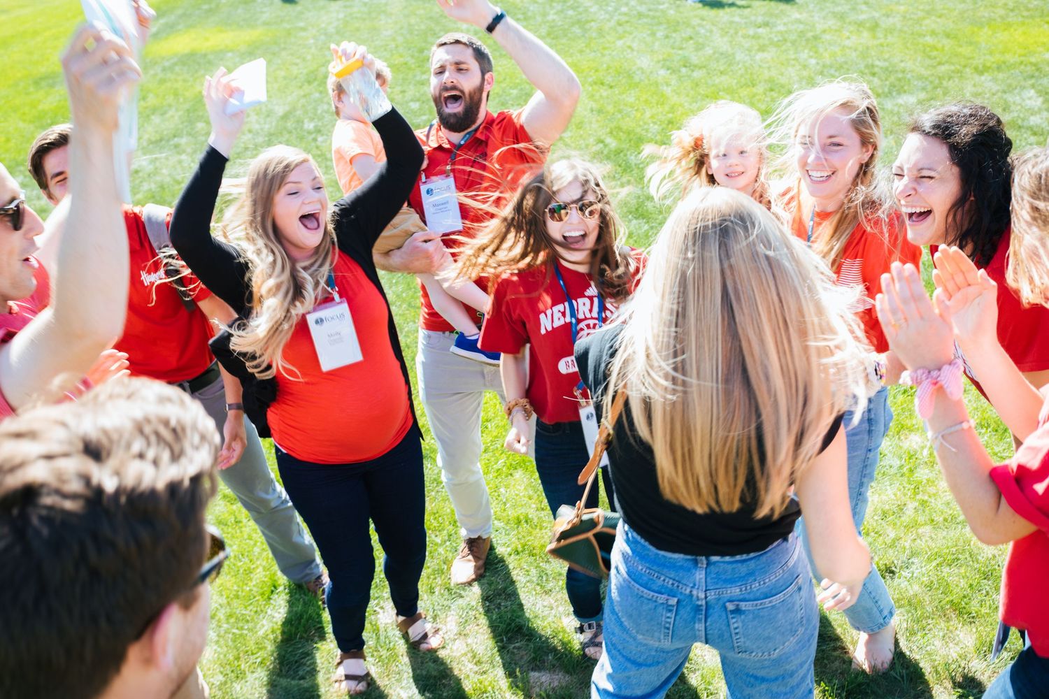 A group of people wearing red shirts dance and celebrate together on a grassy lawn during an outdoor event.