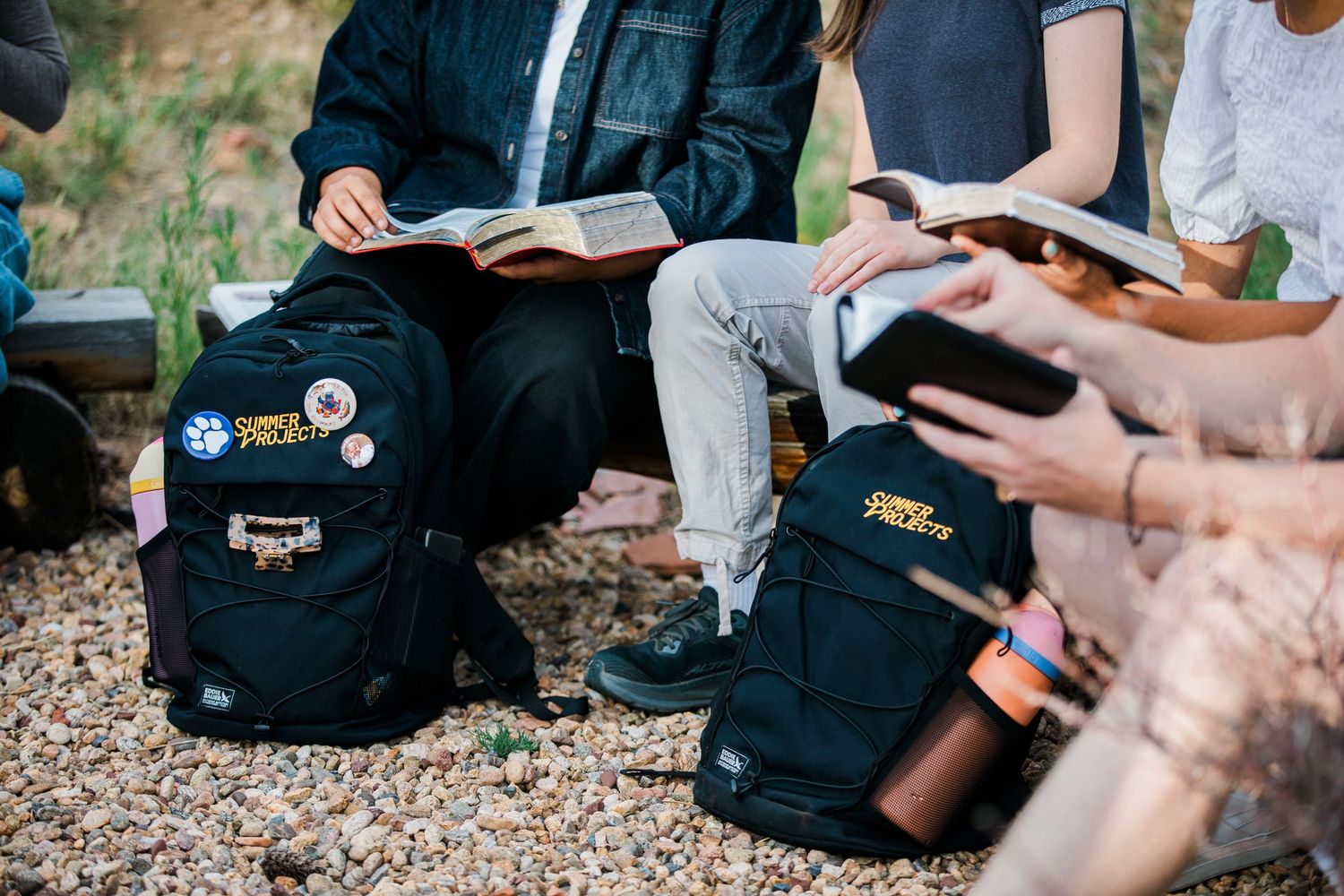 Students sitting outdoors reading Bibles with Young Life backpacks during a group Bible study.