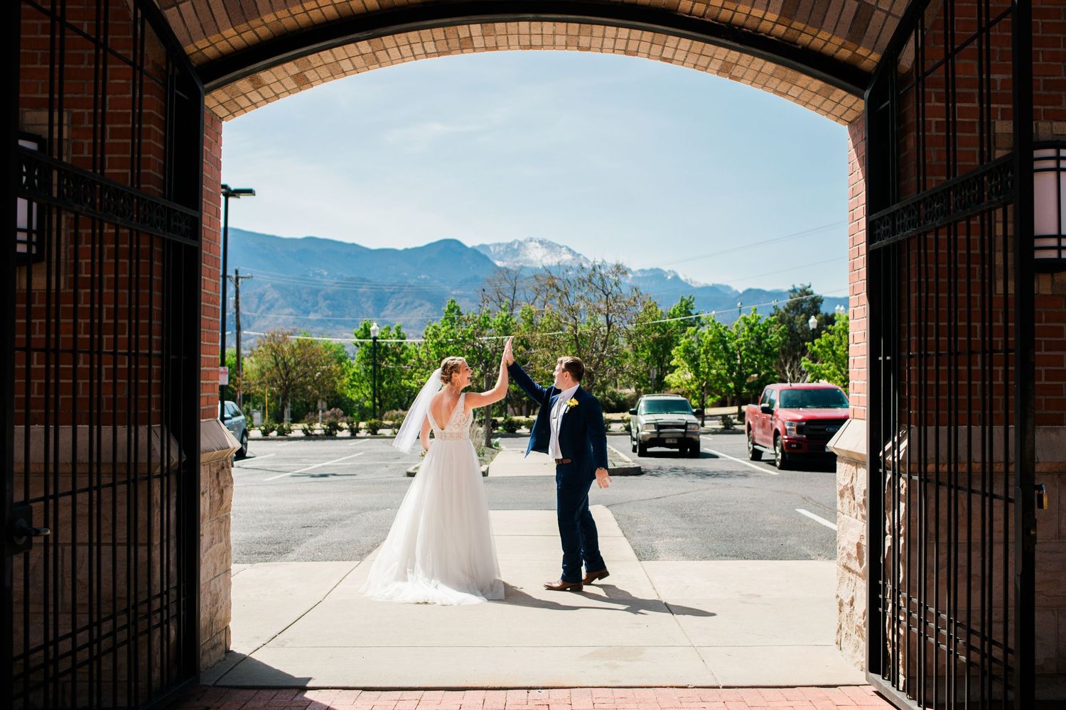 Bride and groom dancing under brick archway with Rocky Mountain backdrop on sunny wedding day.