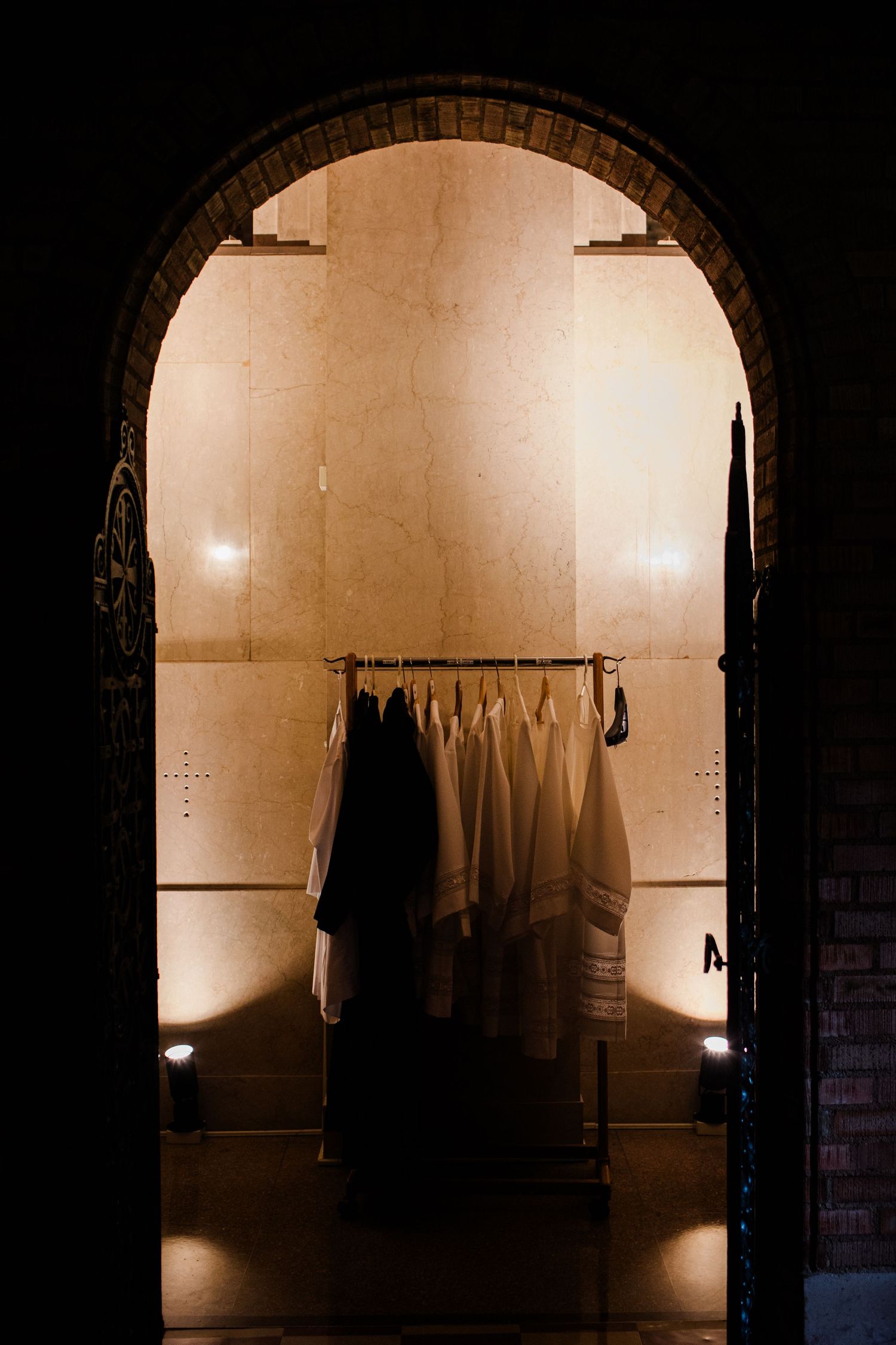 Arched hallway with clothes hanging on a rack illuminated by warm lighting creating moody atmosphere.