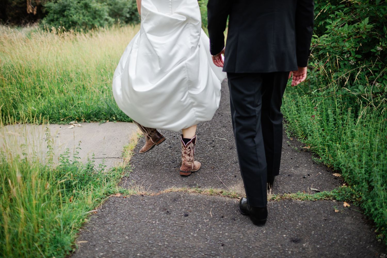 A couple walking down a gravel path surrounded by lush green grass and wildflowers.