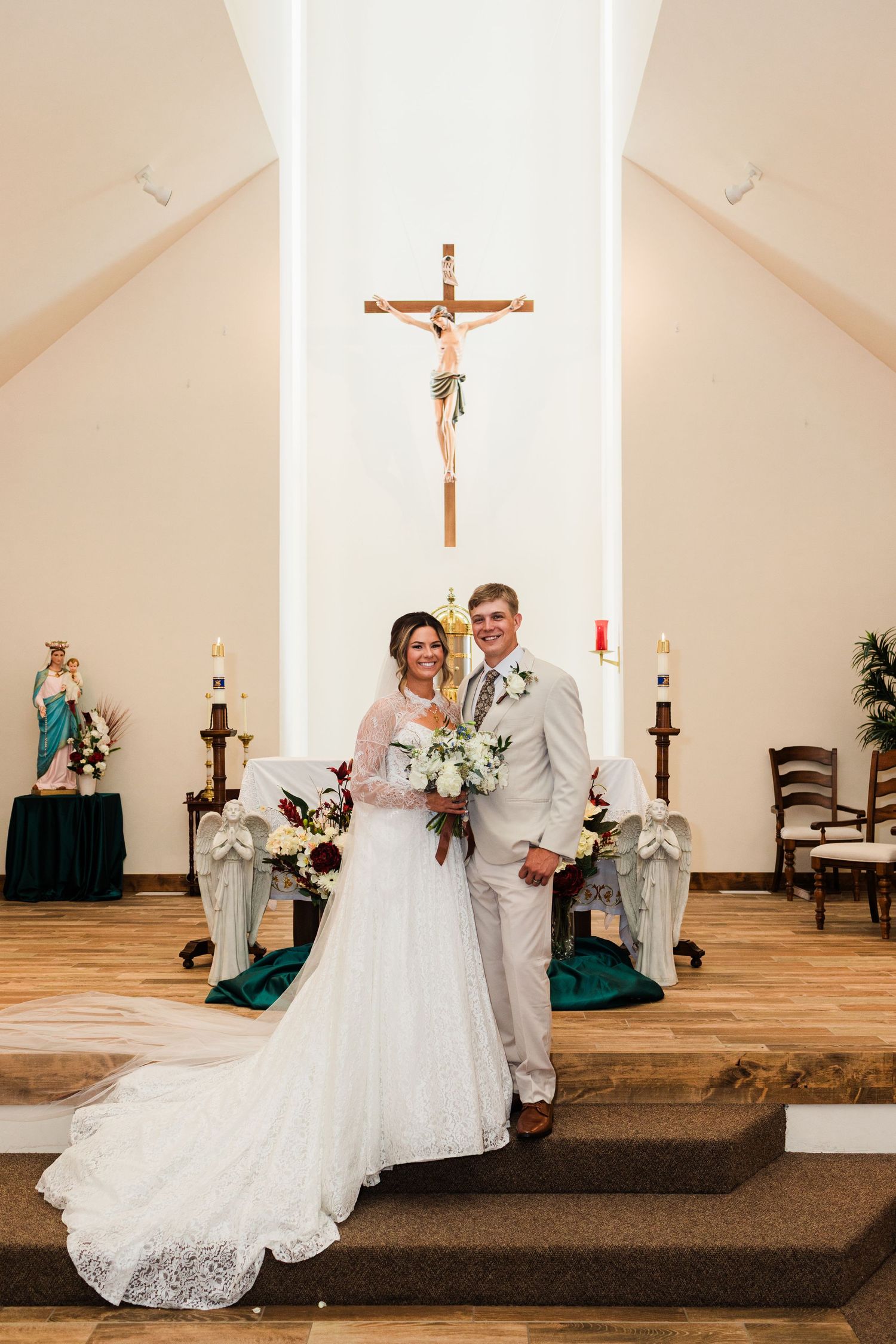 Bride and groom posing together at the altar of a Catholic church with a crucifix and candles in the background.
