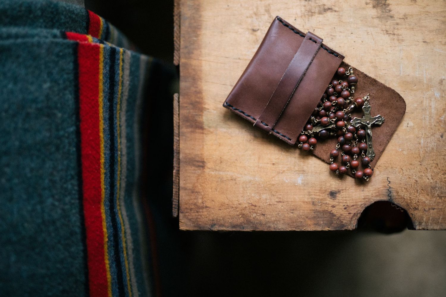 Brown leather wallet sits on rustic wooden surface with scattered coffee beans creating an artisanal composition.