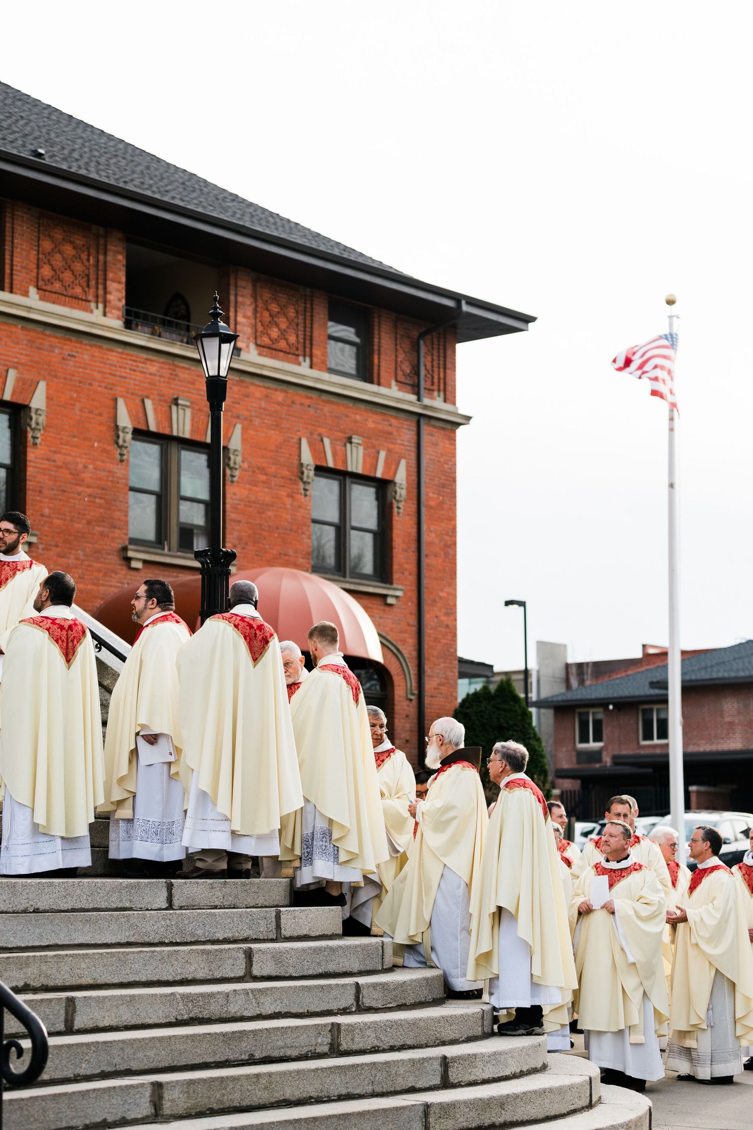 Group wearing cream-colored robes gathered on brick building steps.