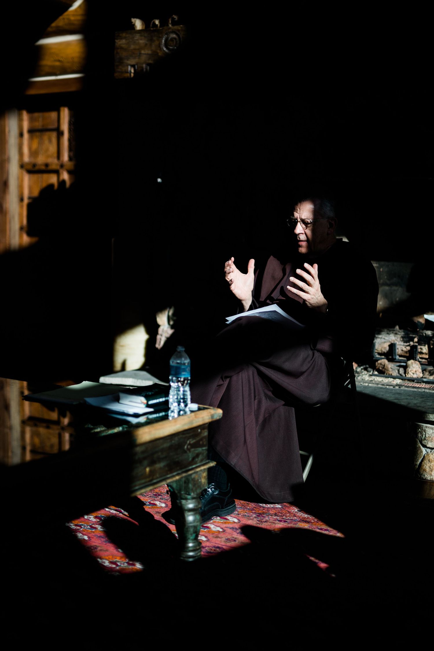 Dark interior scene with figures seated in dim lighting.