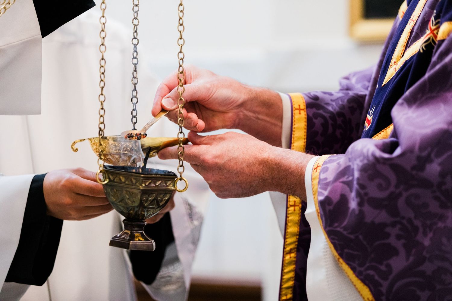 Two hands pass an ornate gold incense burner on chains during a religious ceremony.